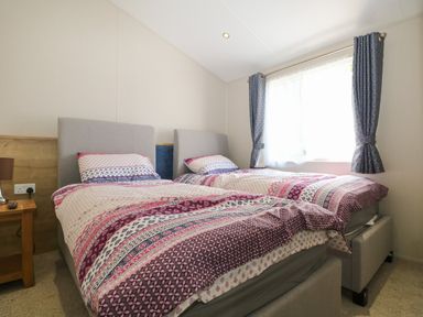 A bedroom with two single beds side by side and a wooden nightstand by the wall at The Goodwood Lodge in Runcton near Chichester