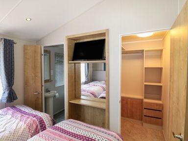A bedroom with two beds a wall-mounted TV a mirror a bathroom to the left and a closet to the right at The Goodwood Lodge in Runcton near Chichester