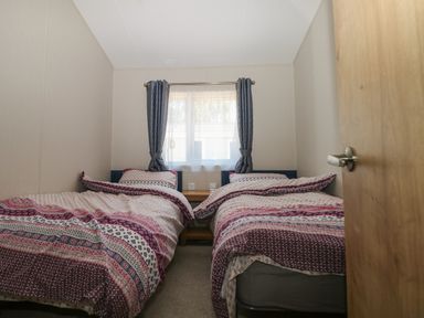 A bedroom with two single beds and a window with curtains at The Goodwood Lodge in Runcton near Chichester