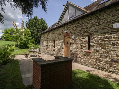 An exterior view of a stone house with a wooden door a picnic table on a paved patio and trees in the background at The Coach House in Ludlow