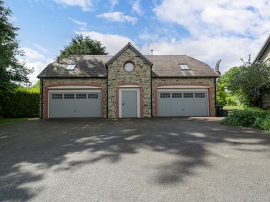 A stone building with two garage doors and a central door with a driveway in front at The Coach House in Ludlow