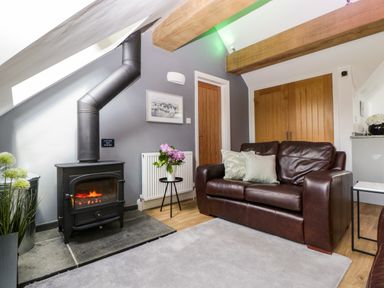 A living room with a wood stove a brown leather sofa and wooden doors at The Coach House in Ludlow