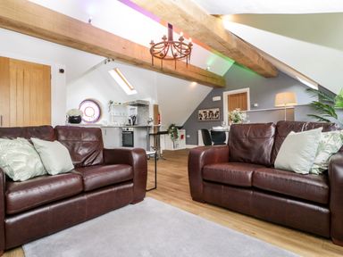 A living room with two brown leather sofas and green pillows open to a kitchen and dining area at The Coach House in Ludlow