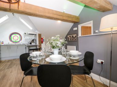 A dining area with a round glass table set with white dishes and glasses surrounded by black chairs in an open kitchen space at The Coach House in Ludlow