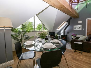 A dining area with a glass table set for four near a living room with a wood stove and leather sofas at The Coach House in Ludlow