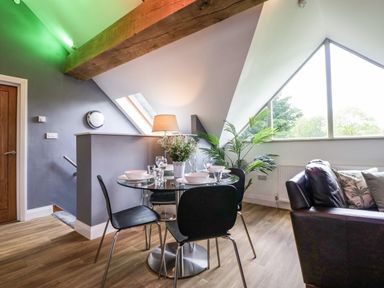 A dining area with a glass table set for four and black chairs next to a window and a brown leather sofa in a room at The Coach House in Ludlow