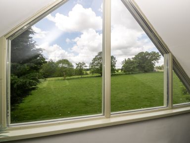 A triangular window showing a green field with trees under a cloudy sky at The Coach House in Ludlow