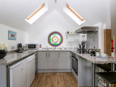 A kitchen with grey cabinets a round stained glass window two skylights and wooden floor at The Coach House in Ludlow