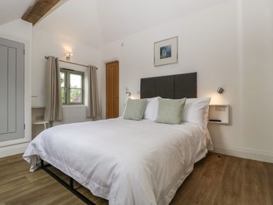 A bedroom with a bed with white bedding two pillows a window with curtains and a wooden door at The Coach House in Ludlow