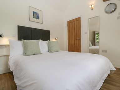 A bedroom with a large bed white bedding two pillows a wooden door a wall mirror and a window at The Coach House in Ludlow