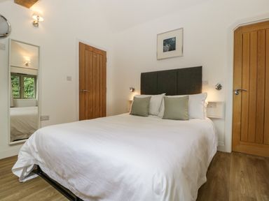 A bedroom with a double bed with white linens two wooden doors and a wall mirror at The Coach House in Ludlow
