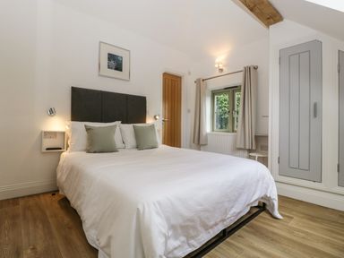 A bedroom with a double bed two green pillows wooden floor and a window with curtains at The Coach House in Ludlow
