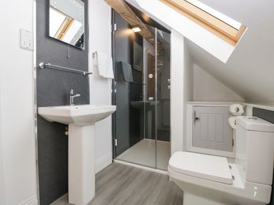 A bathroom with a sink, toilet, glass shower enclosure, towel rack, skylight window and small cupboard at The Coach House in Ludlow