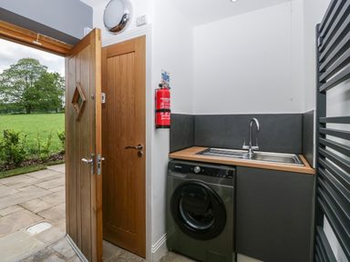 A utility room with a washing machine sink wooden door and fire extinguisher at The Coach House in Ludlow