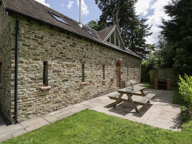An outdoor patio area with a wooden picnic table and benches next to a stone building at The Coach House in Ludlow