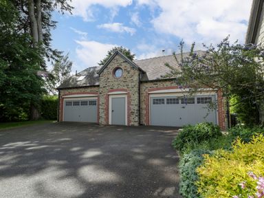 A stone building with two grey garage doors and a middle door surrounded by plants and trees at The Coach House in Ludlow