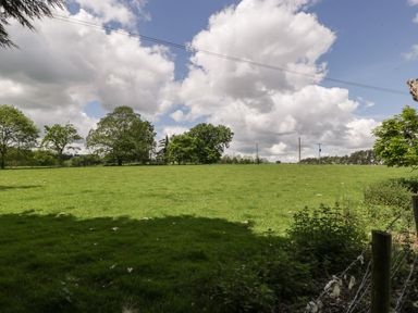 A green field with trees and a wire fence under a cloudy sky at The Coach House in Ludlow