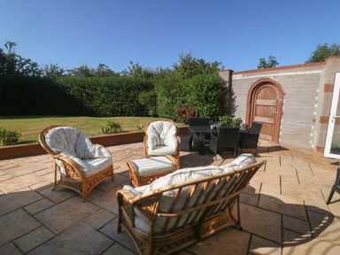 An outdoor patio with rattan seating and a table set near a brick wall and wooden door at Plas Eithin in Mynydd Mechell near Llanfechell