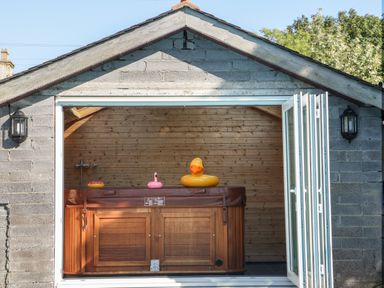 An outdoor wooden hot tub with inflatable toys inside a shed with open folding glass doors at Plas Eithin in Mynydd Mechell near Llanfechell