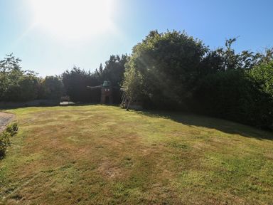 A grassy lawn area with trees and bushes around it at Plas Eithin in Mynydd Mechell near Llanfechell