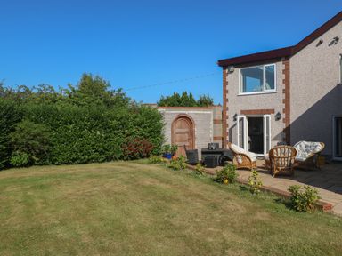 A backyard with lawn and patio furniture next to a house at Plas Eithin in Mynydd Mechell near Llanfechell