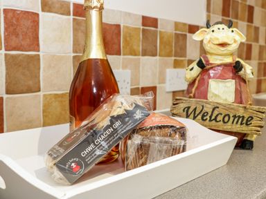A kitchen counter with a bottle of sparkling wine a package of cakes and a cow figurine holding a welcome sign at Plas Eithin in Mynydd Mechell near Llanfechell