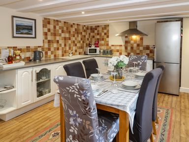 A kitchen with dining table and chairs set with plates and glasses at Plas Eithin in Mynydd Mechell near Llanfechell