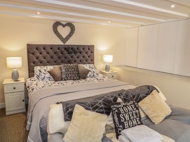 A bedroom with a bed a tufted headboard bedside tables with lamps and decorative pillows at Plas Eithin in Mynydd Mechell near Llanfechell