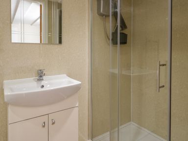 A bathroom with a white sink and cabinet and a shower with glass doors at Plas Eithin in Mynydd Mechell near Llanfechell