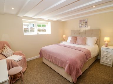 A bedroom with a double bed pink bedding armchair and bedside tables with lamps at Plas Eithin in Mynydd Mechell near Llanfechell