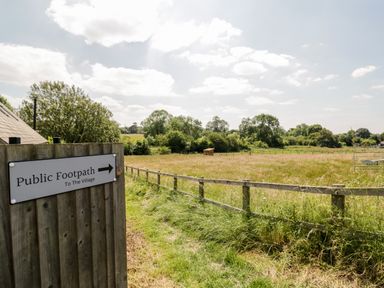 A grassy field with a wooden fence and a sign indicating a public footpath to the village at Oak Lodge At Bridge Lake Farm & Fishery in Chacombe