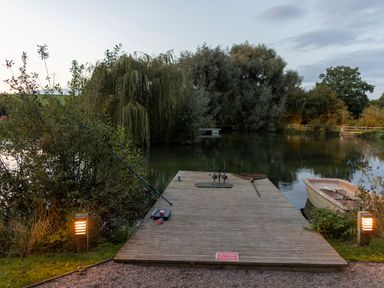 A wooden dock on a lake with fishing rods a net and a small boat at Oak Lodge At Bridge Lake Farm Fishery in Chacombe