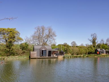 A lakeside wooden lodge with trees around at Oak Lodge At Bridge Lake Farm & Fishery Chacombe