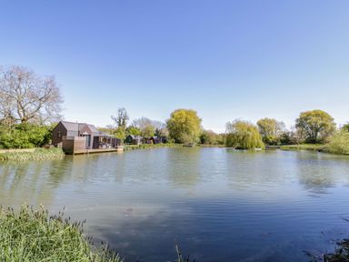 A lake with cabins and trees at Oak Lodge At Bridge Lake Farm & Fishery, Chacombe