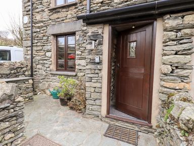 The entrance to a stone house with a wooden door and a window next to it at The Curious Orange in Troutbeck