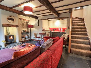 A living room with a red sofa a glass dining table a wood stove and carpeted stairs at The Curious Orange in Troutbeck