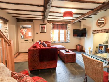 A living room with wooden beams red sofa wood stove and wall mounted tv at The Curious Orange in Troutbeck