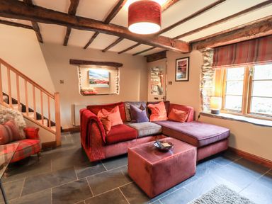 A living room with a sectional sofa table and armchair near a window at The Curious Orange in Troutbeck