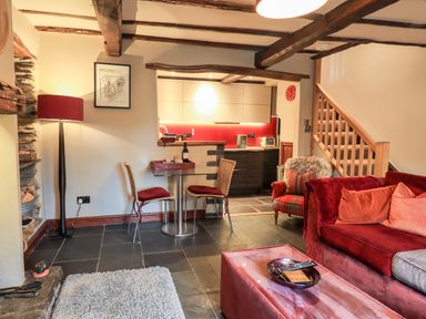 A living room with a red sofa a small dining table with two chairs and a kitchen in the background at The Curious Orange in Troutbeck