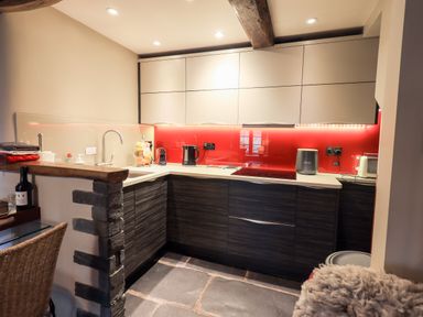 A kitchen with dark lower cabinets white upper cabinets red backsplash and stone floor at The Curious Orange in Troutbeck