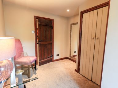 A room with a wooden door a beige closet a glass table a pink chair and a tall mirror at The Curious Orange in Troutbeck