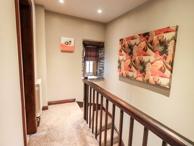 A staircase landing with carpet a wooden railing a small window with a stone frame and two pieces of wall art at The Curious Orange in Troutbeck