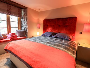A bedroom with a large bed red headboard and window seat with cushions and towels at The Curious Orange in Troutbeck
