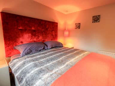 A bedroom with a large bed with gray and orange bedding a red headboard a hanging lamp and two floral wall decorations at The Curious Orange in Troutbeck