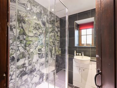 A bathroom with a glass shower enclosure white sink and a window with a red blind at The Curious Orange in Troutbeck