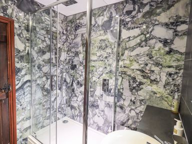 A bathroom with a glass shower enclosure and marble patterned walls at The Curious Orange in Troutbeck