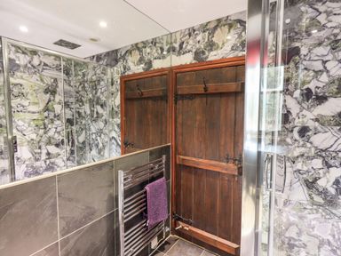 A bathroom with a wooden door a glass shower enclosure and a towel rack with a purple towel at The Curious Orange in Troutbeck