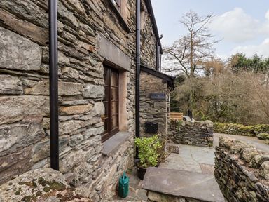 Stone exterior wall of a building with a window plants and a watering can near the entrance at The Curious Orange in Troutbeck