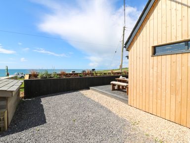 An outdoor area with gravel and a wooden patio next to a wooden building overlooking the sea at Sandpiper Chalet in Eype