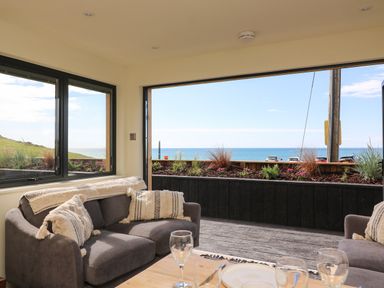 A sitting area with gray sofas and patterned cushions overlooking the ocean at Sandpiper Chalet in Eype